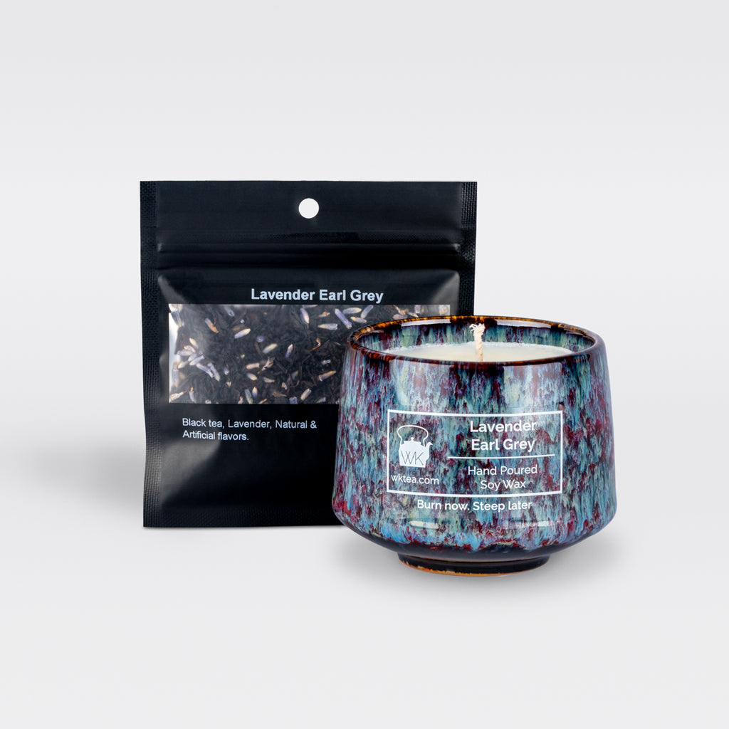 A  blue and purple marbled teacup filled with wax and wick is next to a black resealable pouch of loose-leaf tea. Both items are labeled as “Lavender Earl Grey.”