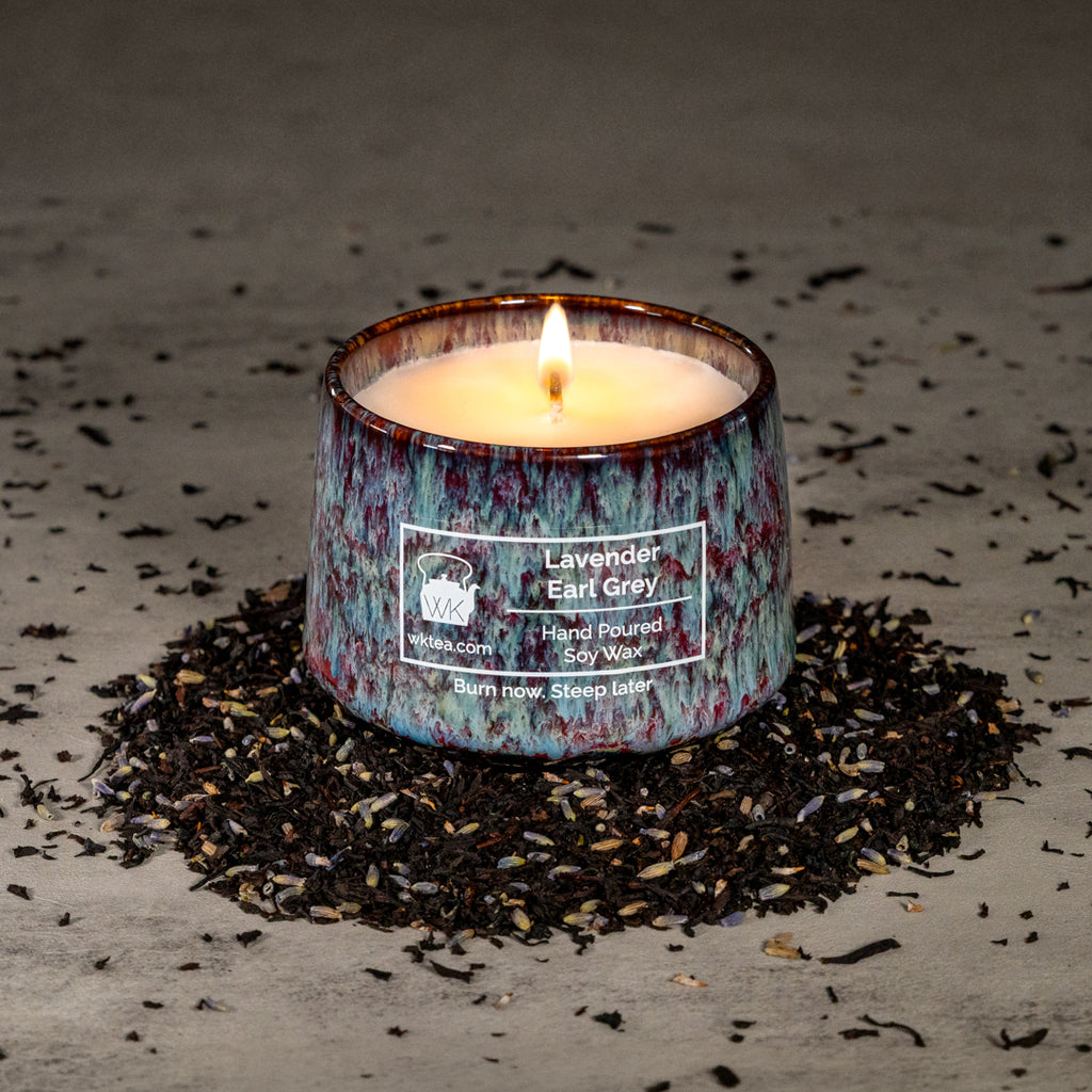 A lit candle in a textured blue and purple marbled ceramic tea cup, surrounded by a ring of black tea leaves and lavender petals