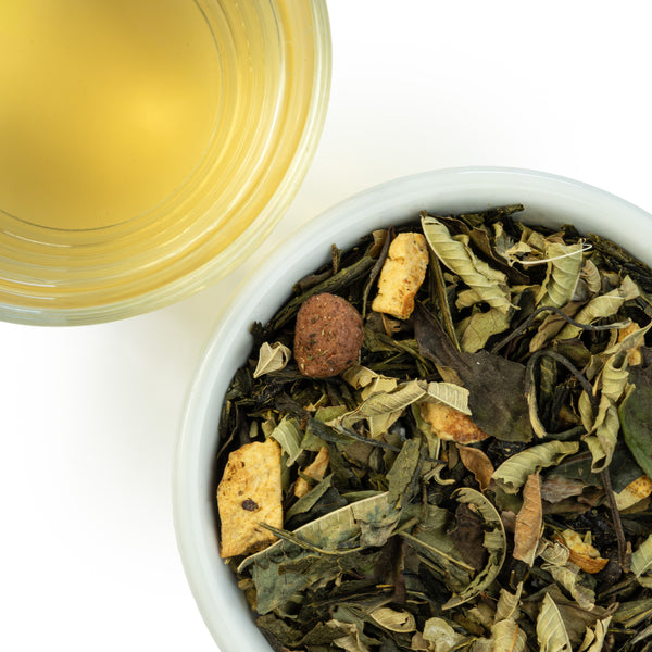 A yellow steeped cup of Lemon Cherry green and white tea next to a bowl of loose leaf Lemon Cherry tea containing green tea, white tea, lemon peel, lemon verbena, pineapple cubes, and sour cherry