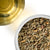 Overhead photo of dried Lemongrass cut into small pieces in a white bowl, paired with a cup of golden herbal tea.