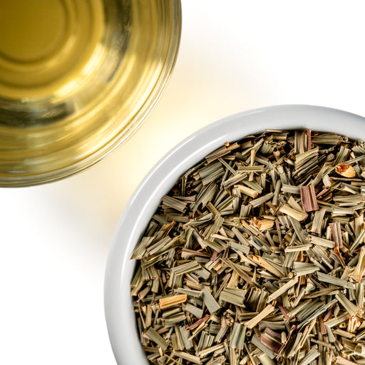 Overhead photo of dried Lemongrass cut into small pieces in a white bowl, paired with a cup of golden herbal tea.