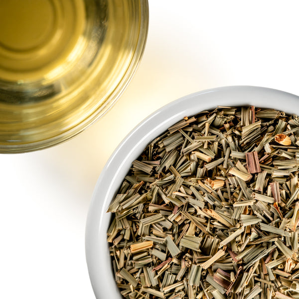 Overhead photo of dried Lemongrass cut into small pieces in a white bowl, paired with a cup of golden herbal tea.