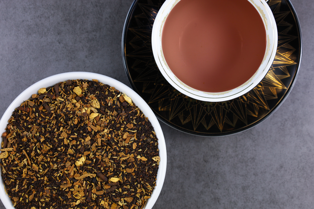 A cup of brewed Masala Chai next to a bowl of tea leaves