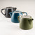 Three ceramic teapots in black, blue, and green on a white background.