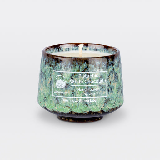 A  candle and wick inside a handmade green and brown marbled tea cup, labeled “Pistachio White Chocolate.” "Burn now. Steep Later." is the product's tagline