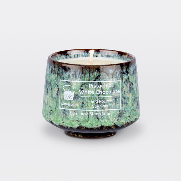 A  candle and wick inside a handmade green and brown marbled tea cup, labeled “Pistachio White Chocolate.” "Burn now. Steep Later." is the product's tagline