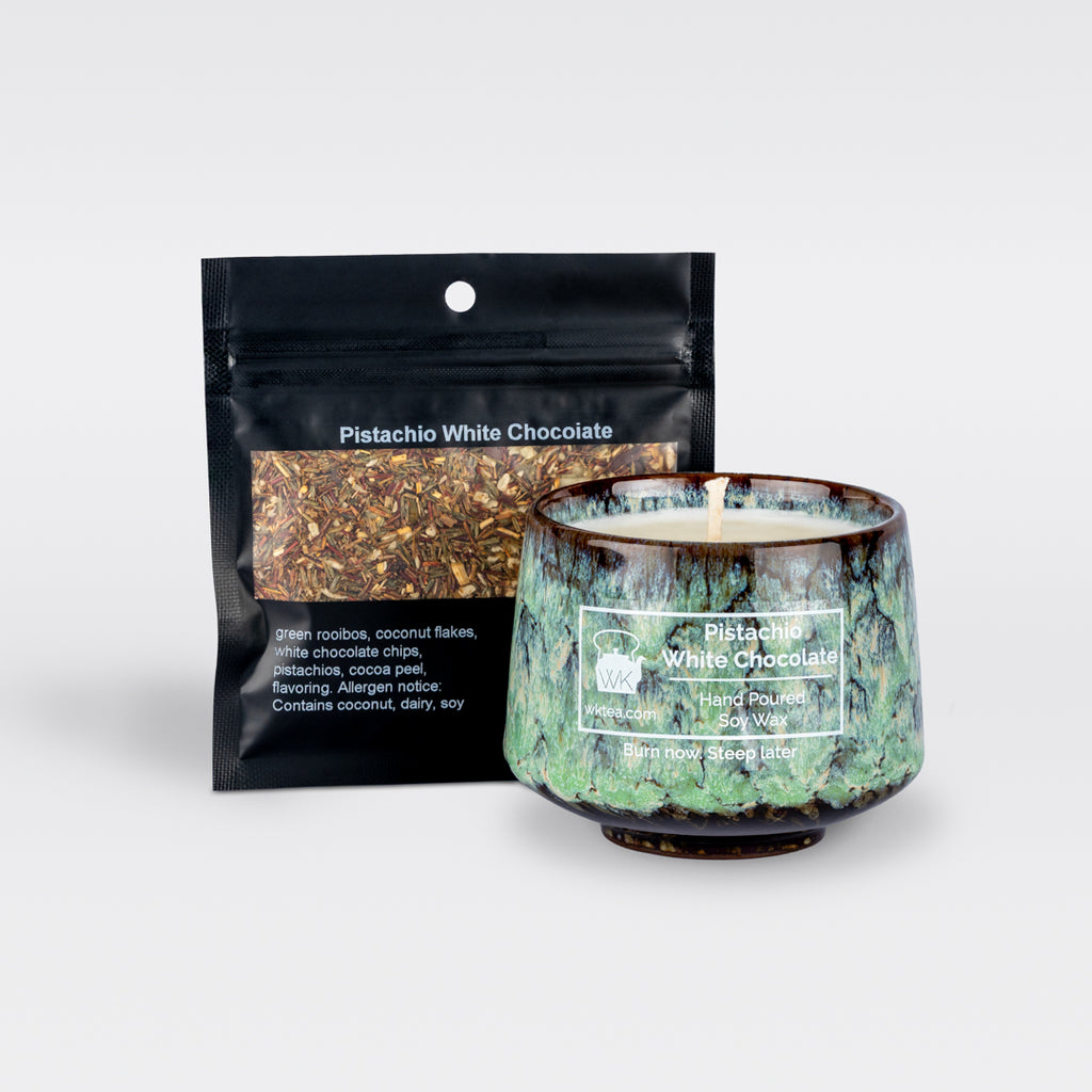 A  green and brown marbled teacup filled with wax and wick is next to a black resealable pouch of loose-leaf tea. Both items are labeled as “Pistachio White Chocolate.”