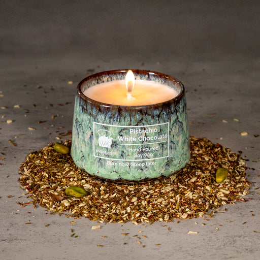 A lit candle in a textured green and brown marbled ceramic tea cup, surrounded by a ring of tea leaves and  pistachio nuts