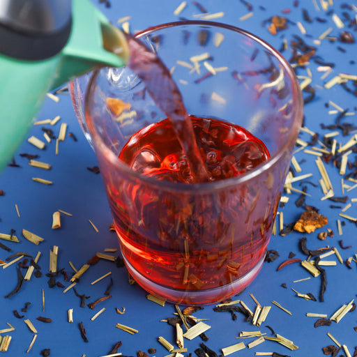 Purple Punch tea being poured into glass next to Purple Punch tea leaves.