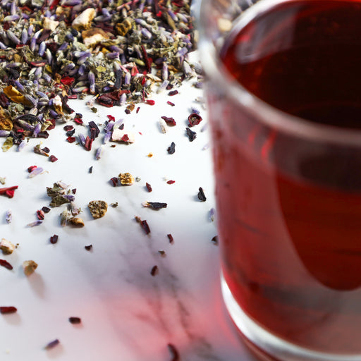 Glass of Raspberry Lavender tea next to mound of Raspberry Lavender tea leaves.