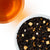 Overhead photo of Salty Caramel Black tea loose-leaves in a bowl with a glass of tea on a white background.