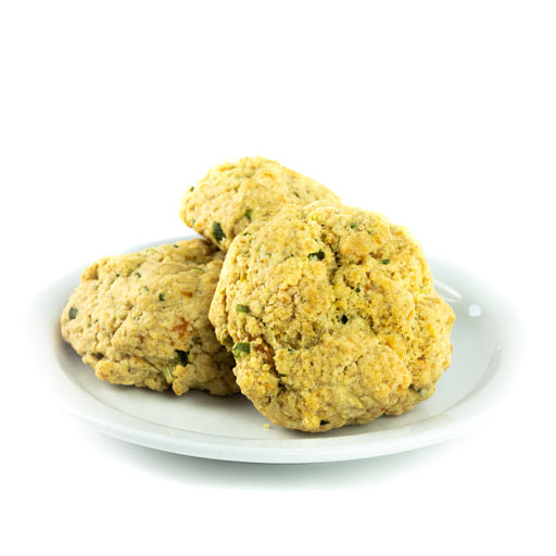Three Savory Herb & Sour Cream scones Lemon Drop scones sit on a white plate. Each scone has a peppering of green herbs, red spices, and yellows pecks of cheese