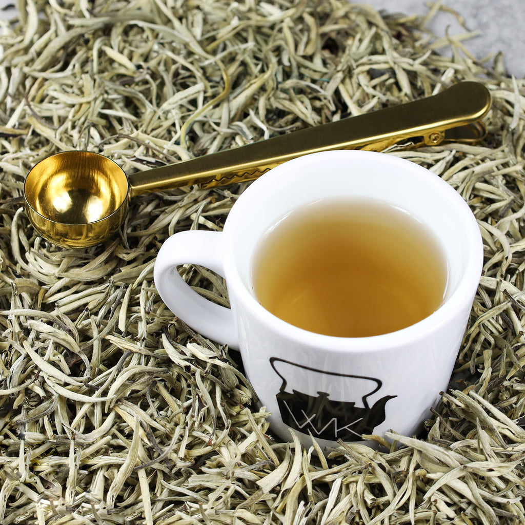 Cup of King of Silver Needles tea in the middle of King of Silver Needles loose leaf tea.