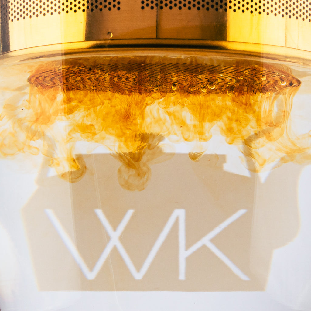 Close-up of loose-leaf tea steeping in a glass mug beneath a stainless steel infuser, creating rich golden swirls in the water