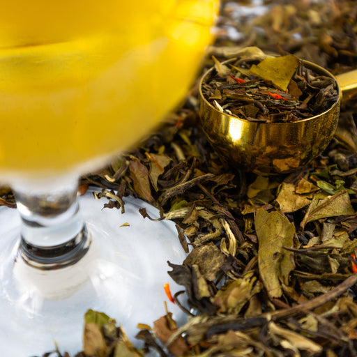 Glass of brewed Sparkling Raspberry Wine next to Gold Tea Scoop filled with Sparkling Raspberry Wine loose leaf tea.