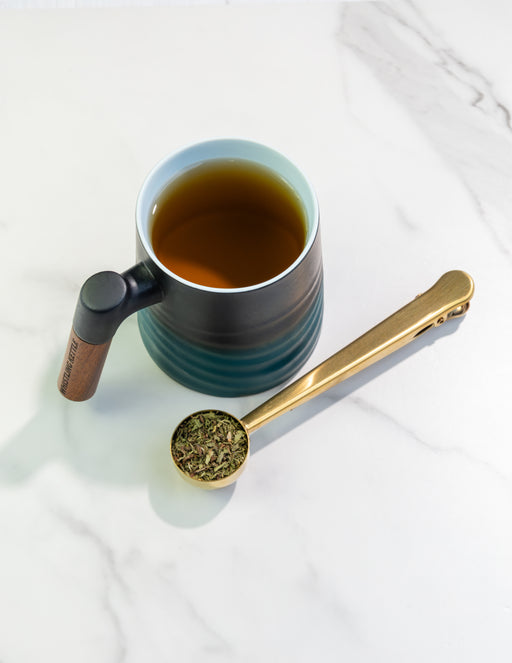 Spearmint Tea in a Wave Mug beside loose-leaf spearmint tea and a golden scoop on a bright marble surface.