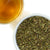 Spearmint leaves in a bowl next to a glass of brewed tea on a white background.