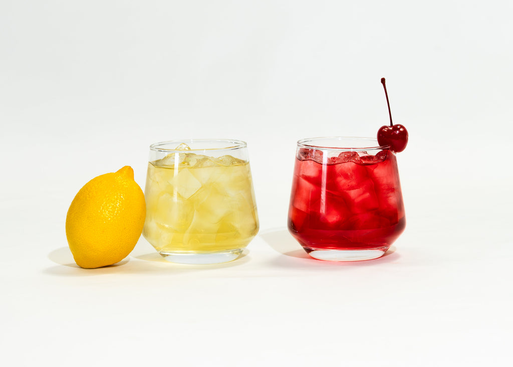 Lemon Cherry green/white iced tea next to a fresh lemon, and Cherry Bomb fruit iced tea with a cherry on top