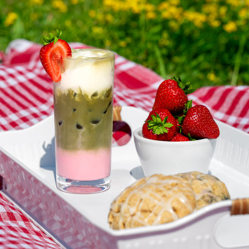Strawberry matcha latte with fresh strawberries and glazed scones on a picnic table