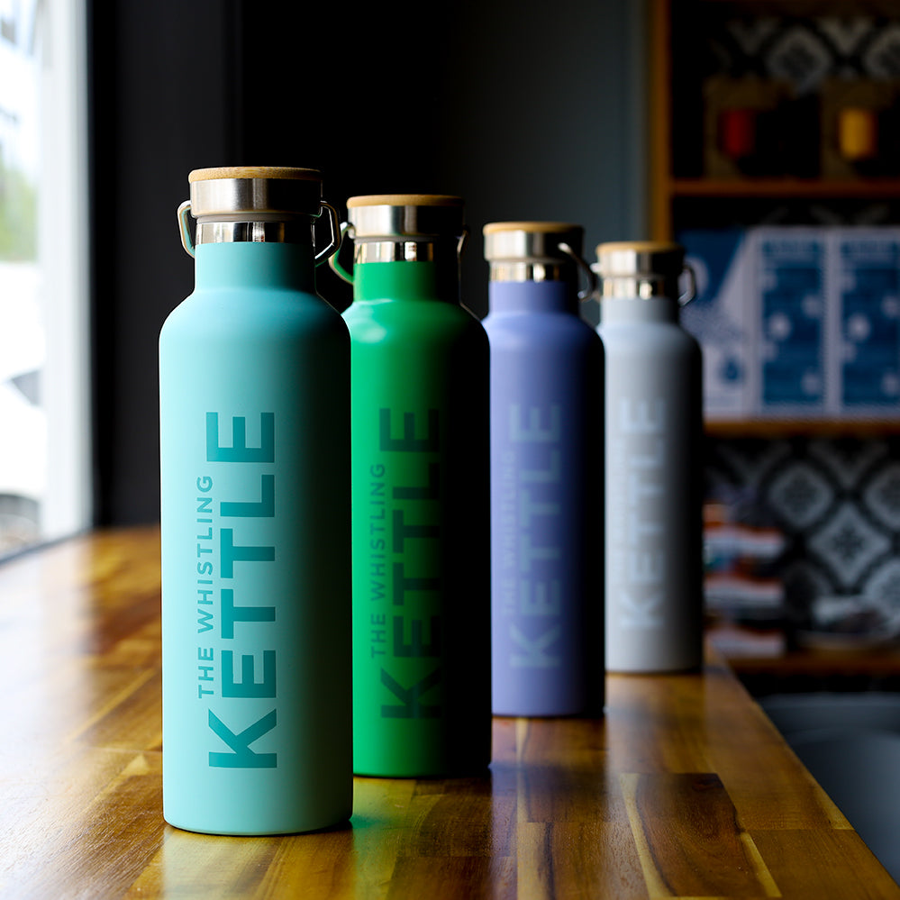Collection of The Whistling Kettle insulated tea flasks in four colors with bamboo-accented lids on a wooden counter