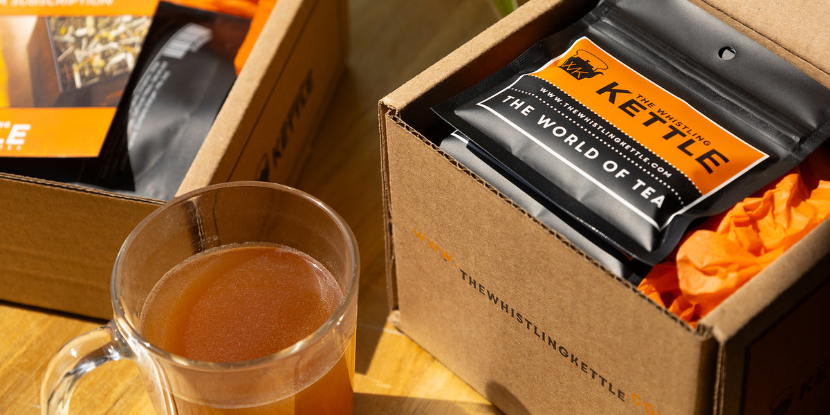 A cup of brewed tea sits next to an opened Tea of the Month club box