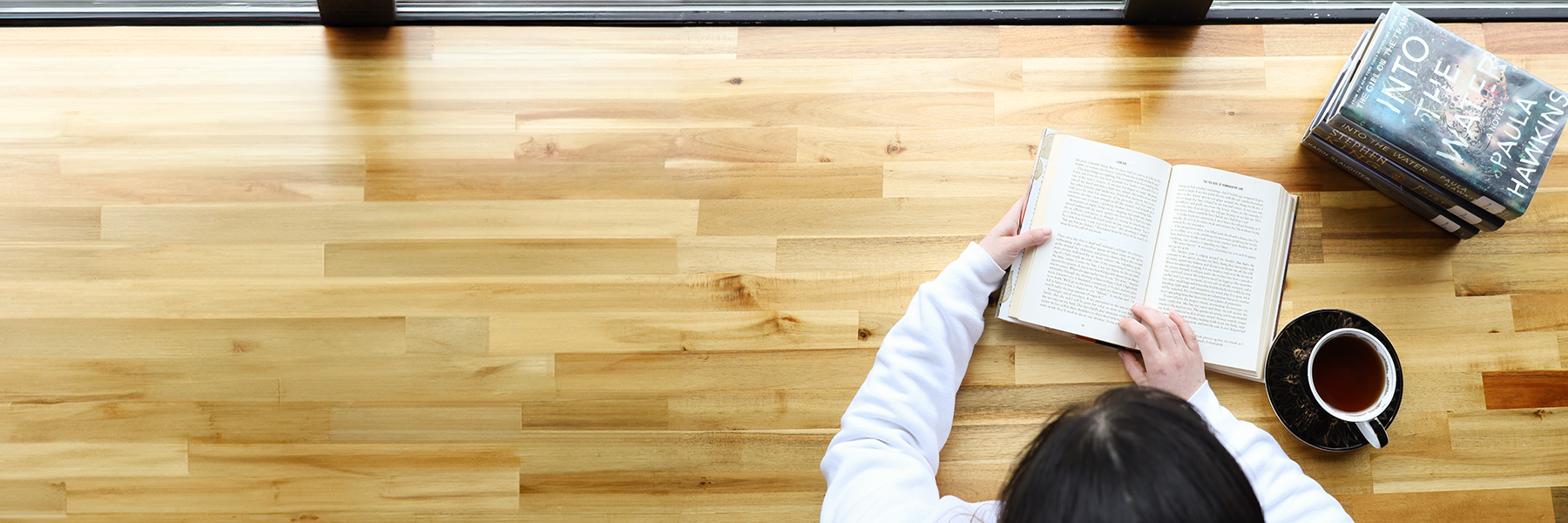 Top-down view of a woman reading a book with a cup of tea at her side.