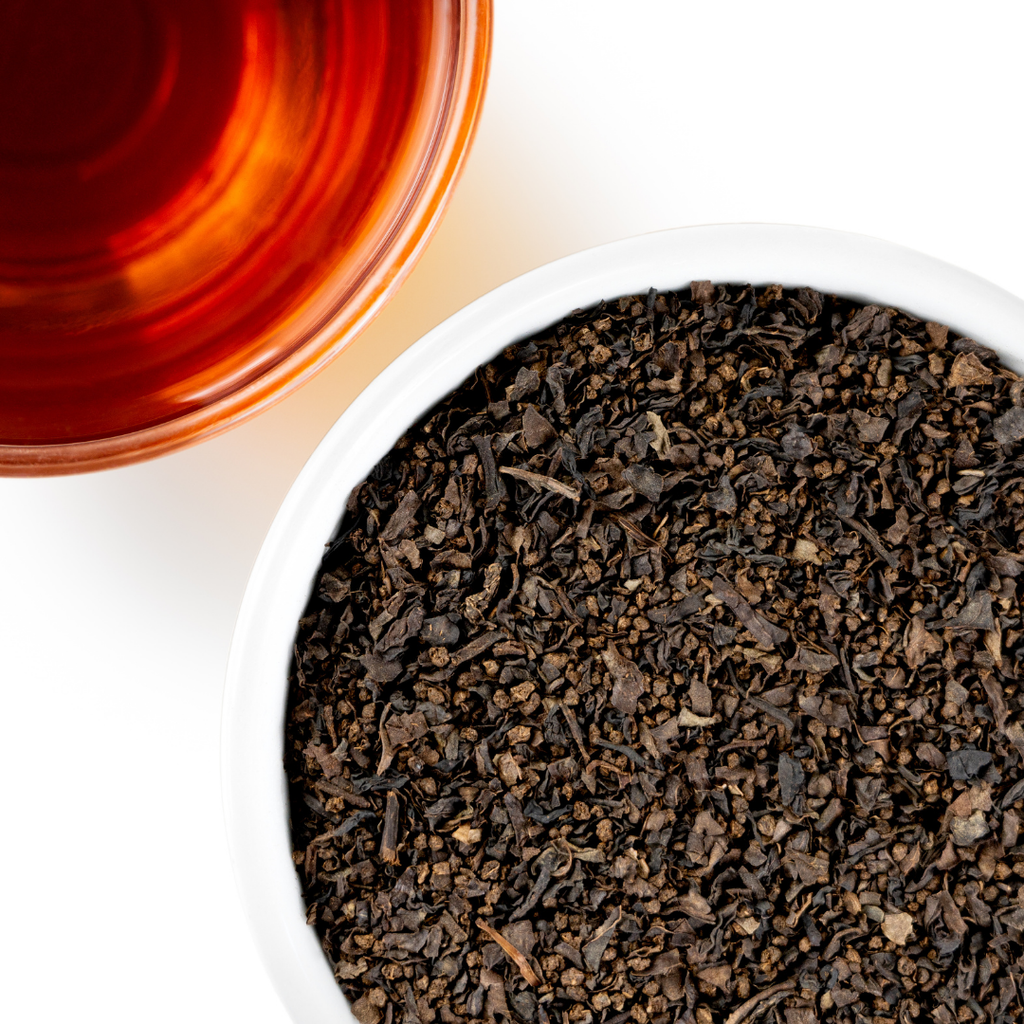 Close-up of a bowl of black tea leaves with a glass of brewed tea on a white background