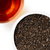 Close-up of a bowl of black tea leaves with a glass of brewed tea on a white background