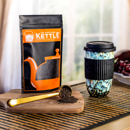 Coffee package, travel mug, and scoop on a wooden board with a blurred background.