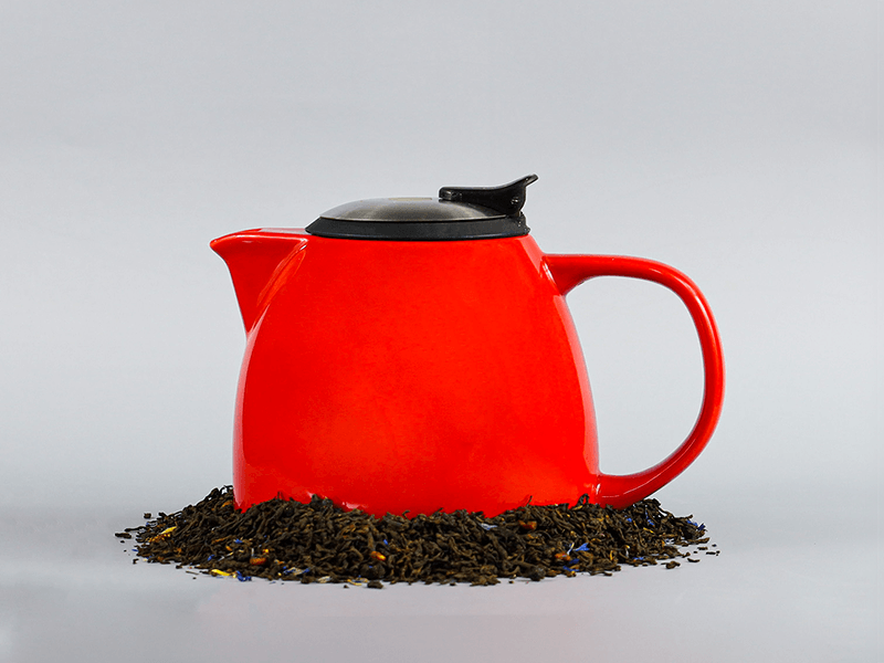 A red tea pot sits on a bed of tea leaves