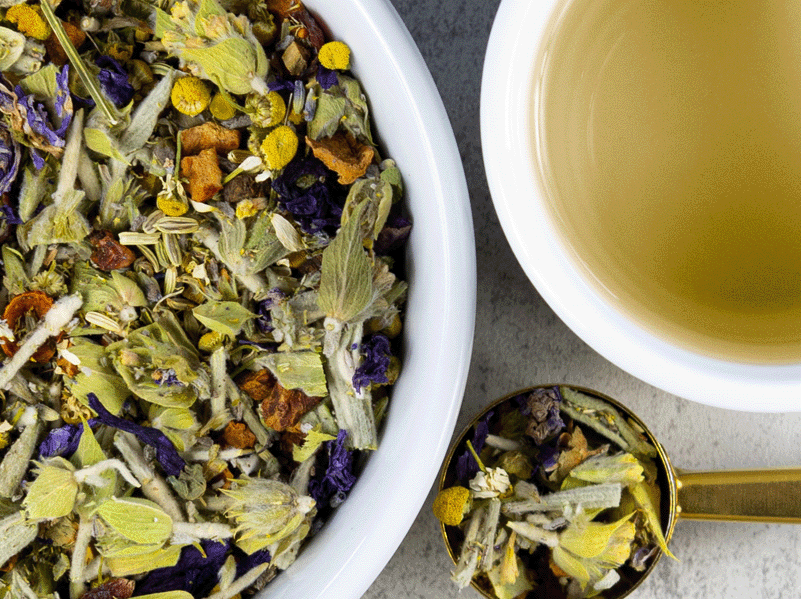A bowl of Greek Mountain Meadow tea leaves next to a cup of brewed tea
